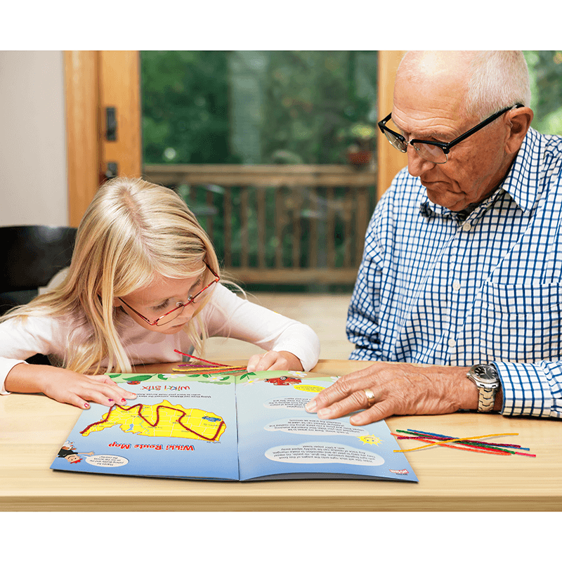 Grandfather and granddaughter playing with the Adventures Across America Activity book at a table.