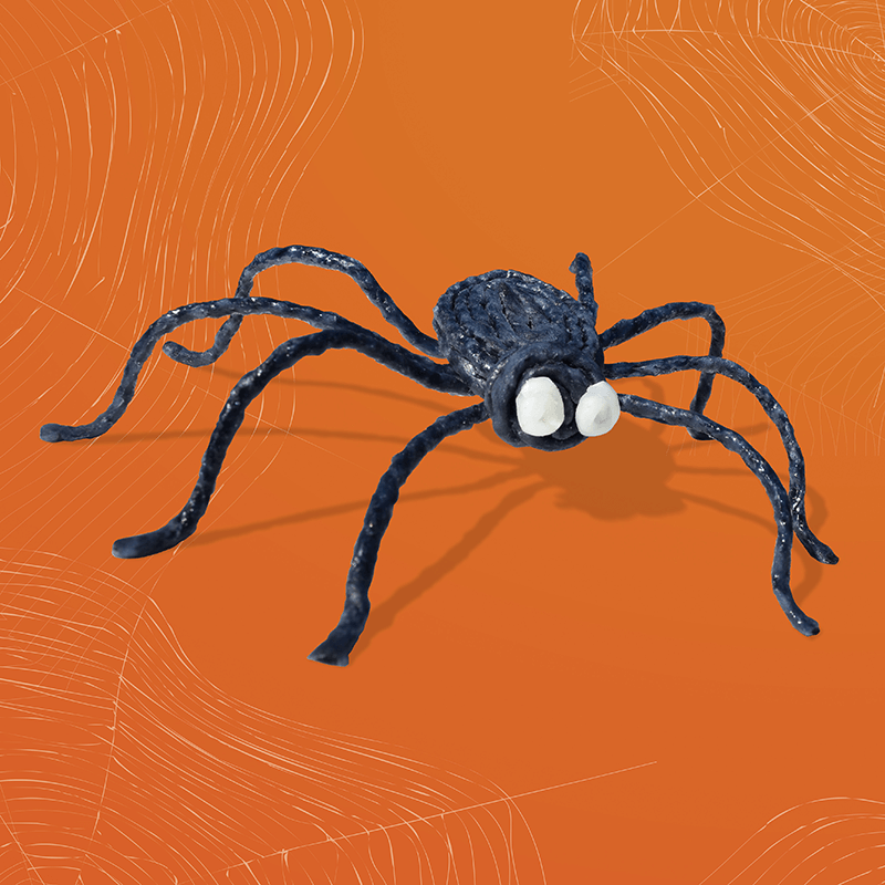 A single spider with white eyes created with Wikki Stix on an orange background.
